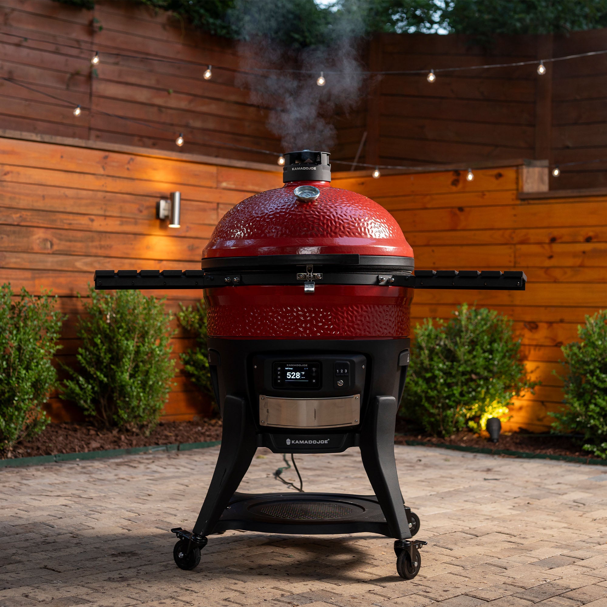 Kamado Joe Big Joe Konnected Joe en fonction sur une terrasse, fumée de cuisson s'échappant du couvercle fermé